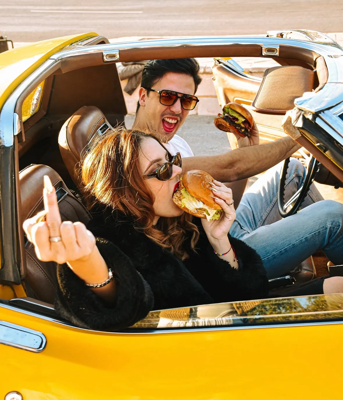 Pareja comiendo burgers de Mr. Majo's en un descapotable amarillo clásico